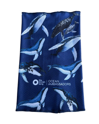 Buff cuello multifuncional The Ocean Lung con protección solar 50+, ballenas jorobadas y delfines sobre fondo azul marino oscuro, Ocean Ambassadors.
Alt text (detalle/doblado): Detalle del logo The Ocean Lung y bordado Ocean Ambassadors en el buff cuello Ballenas, tela mesh técnica azul marino.