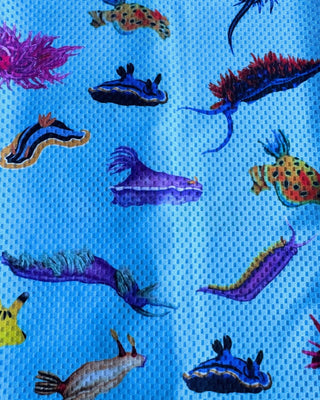 Buff multifuncional The Ocean Lung con estampado de nudibranquios de colores sobre fondo rosa-lila, línea Ocean Ambassadors. Alt text (imagen de detalle/doblado): Detalle de la costura y logo de The Ocean Lung en el buff Nudibranquios Rosa, tela mesh técnica rosa-lila.